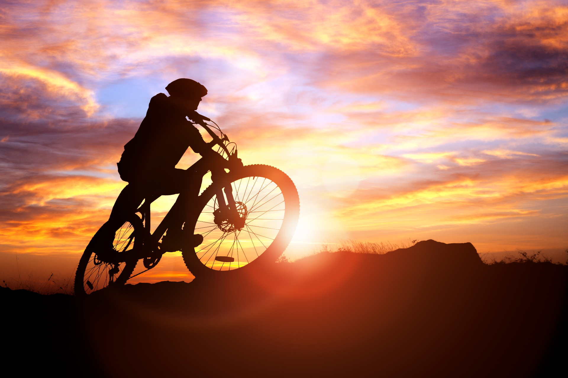 Mountain biker silhouette riding at sunset against a dramatic orange and purple sky