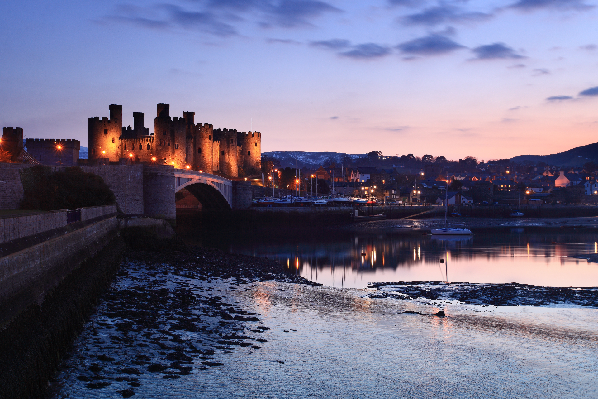 Conwy Castle at dusk, illuminated beside the harbour