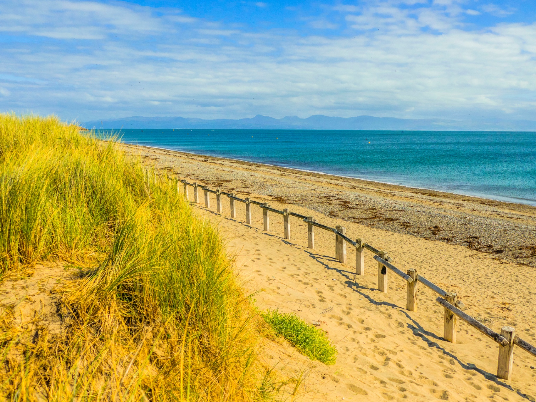 Sandy beach with golden dunes and a wooden boardwalk leading to the sea at Pwllheli