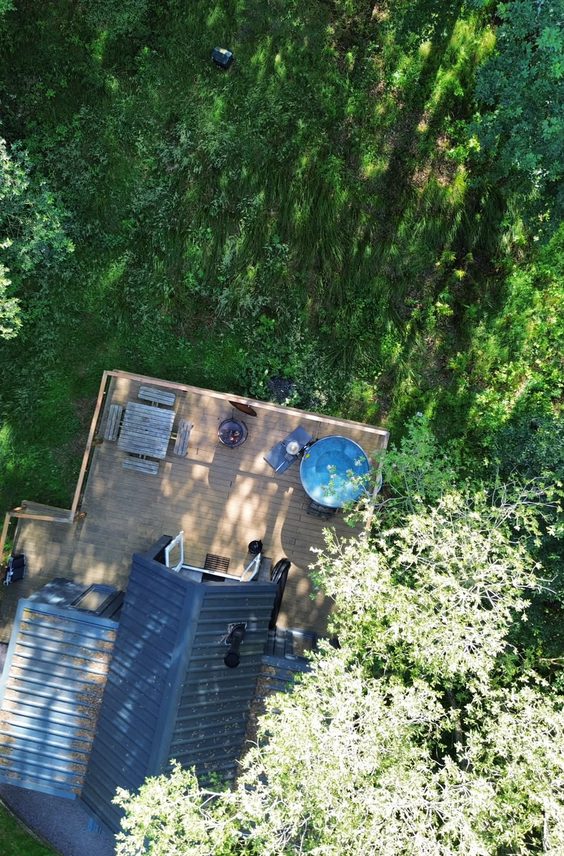 Aerial view of a wooden glamping cabin deck with a wood-fired hot tub surrounded by green woodland